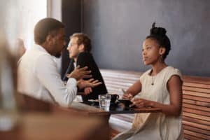 A black man and a black woman talking in a coffee shop.