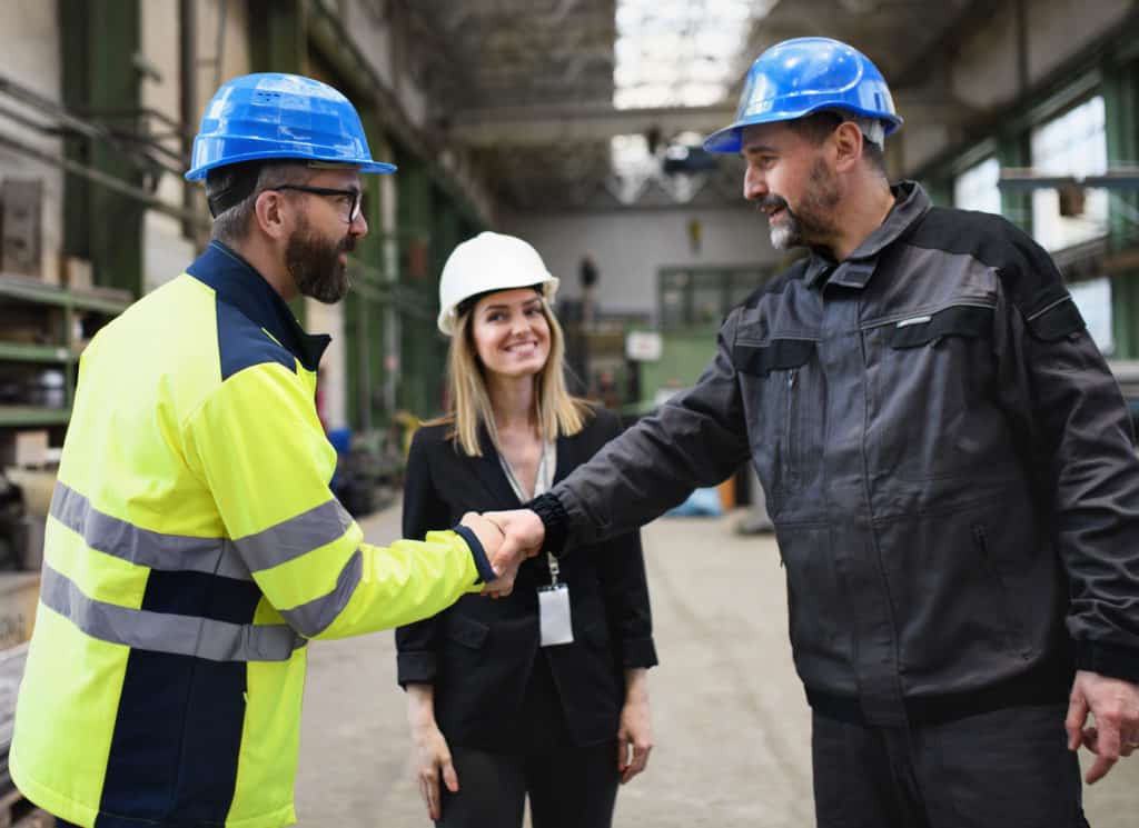 Engineer and industrial worker in uniform shaking hands